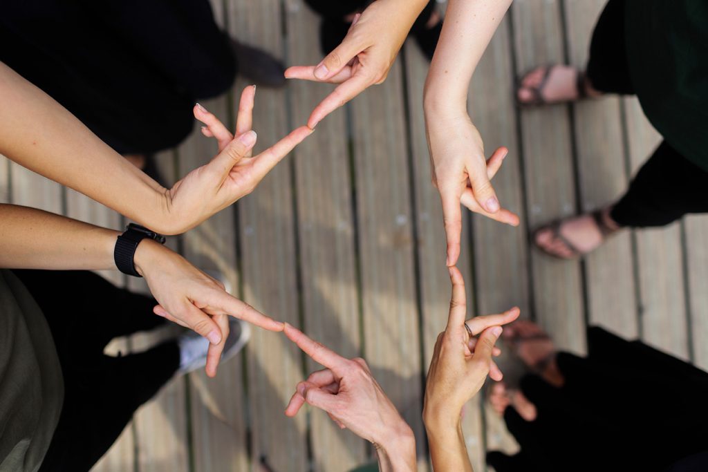 5 Personen bilden mit den Händen und der Gebärde für Kontakt ein Dreieck.